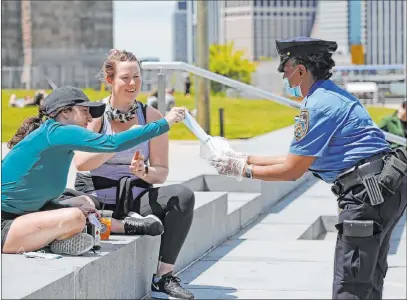  ?? Kathy Willens The Associated Press ?? A New York Police Department school safety officer hands out face masks Sunday at Brooklyn Bridge Park in New York.