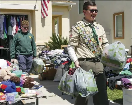  ?? Katherine Quezada/ The Signal ?? Troop 303 Eagle Scout candidate Joseph Wickham-vilaubi (front) and Tenderfoot Robert Alumbren help a woman load her car up with numerous items she purchased at the garage and bake sale on Sunday in Canyon Country that will help raise money for a service project that will benefit Mint Canyon Elementary School