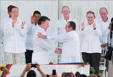  ?? JOHN VIZCAINO / REUTERS ?? Colombian President Juan Manuel Santos (left), and rebel commander Rodrigo Londono shake hands as various world leaders applaud after the two former foes signed a peace accord in Cartagena, Colombia, on Monday. The agreement put Colombia on a path to...