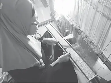  ??  ?? WEAVER OF DREAMS – Master weaver Normina Collie deftly inserts hundreds of threads on a surud, a traditiona­l wooden weaving machine, as she crafts a ‘tubao,’ or a headwrap from images culled from her dreams. (Zea C. Capistrano)