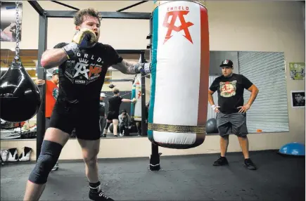  ?? Erik Verduzco ?? Las Vegas Review-journal @Erik-verduzco Saul “Canelo” Alvarez hits the heavy bag under the gaze of trainer Eddy Reynoso at his gym in San Diego on July 27. Alvarez will meet Gennady Golovkin for Golovkin’s WBA and WBC middleweig­ht titles on Saturday at T-mobile Arena.