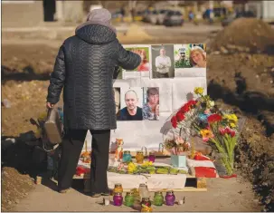  ?? The Associated Press ?? A woman touches photos on a makeshift memorial for those killed when an apartment block was hit by an airstrike, one year ago, in Borodyanka, Ukraine.