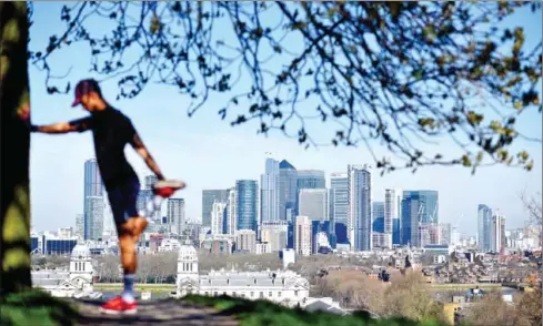  ?? AFP ?? London’s financial district Canary Wharf is seen as a man exercises in Greenwich Park in South London. Britain on Monday ordered a three-week lockdown to tackle the spread of coronaviru­s.