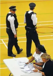  ??  ?? Police officers walk past as votes cast in the general election are counted in Islington in London shortly after the polls closed Thursday.