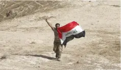  ?? (Thaier Al-Sudani/Reuters) ?? A SHI’ITE FIGHTER holds an Iraqi flag in Makhoul mountains, north of Baiji, Iraq.