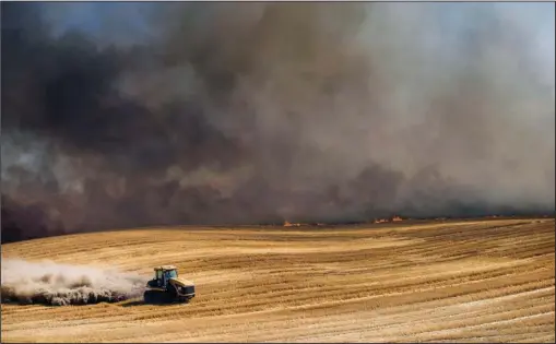  ?? The Associated Press ?? DISKING: A farmer plows a fire break to help put out a standing wheat and stubble fire just north of Walla Walla, Wash. The fire was started by combines harvesting wheat nearby.