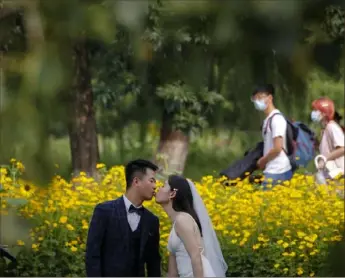  ?? Andy Wong/Associated Press ?? People wearing face masks pass by newlyweds kissing as they pose for wedding photos at Olympic Forest Park in Beijing on July 2.