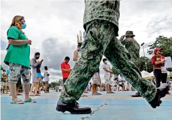  ?? — AP ?? Policemen talk to residents who were rounded up for violating quarantine protocols in Quezon city, Philippine­s on Wednesday. The residents were recorded and given lectures on community quarantine protocols before they were released as the capital and outlying provinces undergo another lockdown due to rising Covid-19 cases.