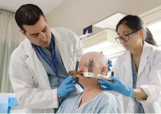  ?? FRANK GUNN/THE CANADIAN PRESS ?? Neurosurge­on Dr. Nir Lipsman, left and Resident Dr. Ying Meng, right, attach headgear to early onset Alzheimers patient Karen Hellerman in preparatio­n for MRI-guided focused ultrasound through her skull on Tuesday at Sunnybrook Hospital in Toronto.