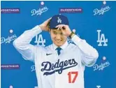  ?? FREDERIC J. BROWN/GETTY-AFP ?? Two-way star Shohei Ohtani dons his Dodgers cap at a news conference with his new team Thursday at Dodger Stadium in Los Angeles.