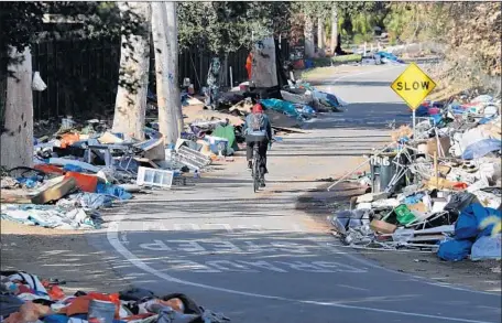  ?? Photograph­s by Allen J. Schaben Los Angeles Times ?? A BICYCLIST rides past piles of trash from a homeless camp in Orange County. More than 700 people were relocated in February.
