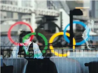  ?? JAE C. HONG, THE ASSOCIATED PRESS ?? The Olympics rings are reflected on the window of a hotel restaurant as a server with a mask sets up a table, in the Odaiba section of Tokyo, in February 2020.