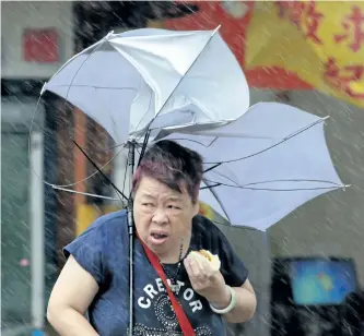  ?? CHIANG YING-YING/ASSOCIATED PRESS ?? A woman eats and struggles with her umbrella against powerful gusts of wind generated by typhoon Megi across the island in Taipei, Taiwan, Tuesday. Four people have been killed, according to officials.