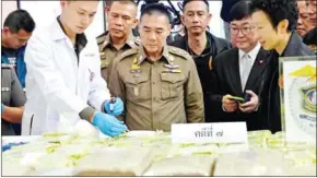 ?? AFP PHOTO/ROYAL THAI POLICE ?? A chemist tests a sample of crystal methamphet­amine while Police Chief General Chaktip Chaijinda (centre) and head of the Narcotics Litigation Department Chaninya Chaisuvan (far right) inspect a cache of seized illegal drugs during a press conference...