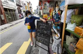  ??  ?? Tending shop: Lee preparing a signboard offering discounts at her clothes-and-souvenirs stall in Armenian Street, Penang.