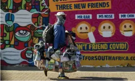  ?? South Africa. Photograph: Themba Hadebe/AP ?? A street vendor walks past a mural on how to prevent the spread of coronaviru­s in Soweto,