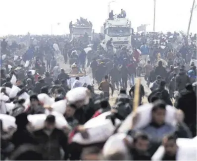  ?? Kosay Al Neme / Reuters ?? Palestinos cargan sacos de harina cerca de un puesto de control israelí, el pasado febrero.