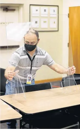  ?? RICARDO RAMIREZ BUXEDA/ORLANDO SENTINEL ?? Giovanny Quero, employee of the Orange County Supervisor of Elections, sets up a plexiglass barrier for early voting in the Community Room of the Winter Park Public Library on July 30.