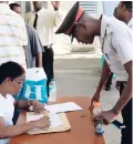  ?? FILE ?? Camille Maragh (left) voting location assistant assisting a police officer at the Greater Portmore police station to locate his name before he voted on Monday February 22, 2016.