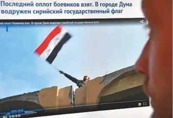  ?? AFP ?? A man looks at a computer screen in Moscow displaying a web page in Russian cyrillic script with a man waving a Syrian flag over a building in the Syrian town of Douma yesterday.