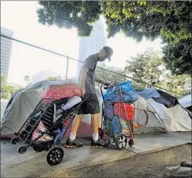  ?? Richard Vogel Associated Press ?? A HOMELESS MAN moves his belongings near Los Angeles City Hall before a cleanup this year. Nearly 1,000 homeless people have died in the county this year.