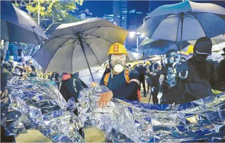  ?? AP-Yonhap ?? Anti-government protesters hold aluminum foil to prevent the police’s blue-colored water cannon in Hong Kong, Saturday. Some protesters targeted government buildings, while police used pepper spray and a water cannon that fired a blue liquid, used to identify protesters, during clashes Saturday.