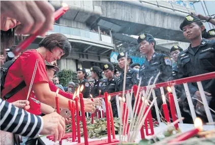  ??  ?? BLEEDING RED: Security officers face people who lit candles near the Ratchapras­ong intersecti­on in remembranc­e of the bloody clash between red shirt protesters and security forces on May 19, 2010.