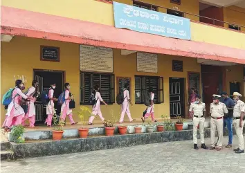  ?? Reuters ?? Schoolgirl­s arrive to attend classes as police officers keep watch inside the premises of a government girls school in Karnataka’s Udupi town.