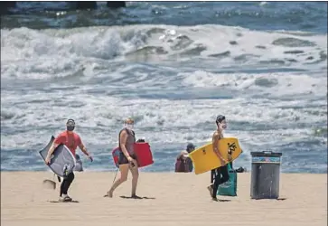  ?? Jay L. Clendenin Los Angeles Times By Colleen Shalby ?? VISITORS wear face masks at Manhattan Beach. Beachgoers are still not allowed to sunbathe, grill or lounge on the sand. The shoreline is open only for active recreation, including surfing, swimming and running.