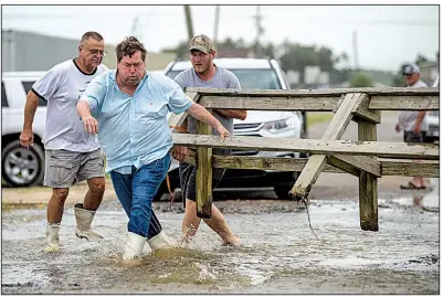  ?? AP/The Advocate/CHRIS GRANGER ?? Louisiana Lt. Gov. Billy Nungesser (center) helps move a wooden barricade to block a road Saturday as water rises in Plaquemine­s Parish just south of New Orleans.