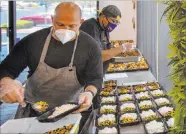  ??  ?? Jeffrey Weiss, left, and Paras Shah, co-owners and cochefs at Valencian Gold, package meals June 26 for the Delivering With Dignity food program.