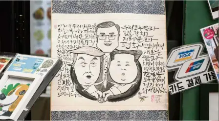  ?? — AFP ?? Artful unity: A cartoon depicting Moon embracing Trump and Kim is displayed at a shopping centre in Seoul.