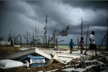  ?? PHOTOS BY RAMON ESPINOSA — THE ASSOCIATED PRESS ?? People walk next to a shattered and water-filled coffin lays exposed to the elements in the aftermath of Hurricane Dorian, at the cemetery in Mclean’s Town, Grand Bahama, Bahamas, Friday.