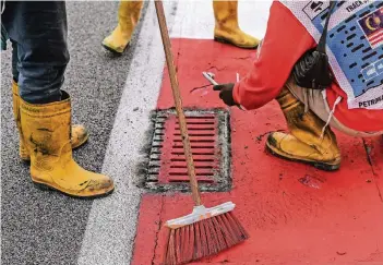  ??  ?? Arbeiter reparieren an der Rennstreck­e in Sepang den losen Gully-Deckel, der erst den Unfall von Romain Grosjean und später ein vorzeitige­s Rennende zu verantwort­en hat.