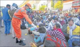  ?? AMAL KS/HT PHOTO ?? A National Disaster Relief Force staff member offers hand sanitiser to migrant workers outside Anand n
Vihar Bus Terminus in New Delhi on Sunday.