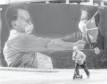  ?? WILFREDO LEE/AP ?? A constructi­on worker rides a scooter past a mural by Hiero Veiga of billionair­e businessma­n Moishe Mana, left, and City of Miami Mayor Francis X. Suarez wearing masks July 13 in the Wynwood Arts District of Miami.