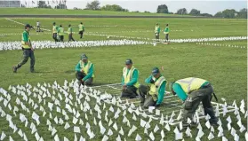  ?? PATRICK SEMANSKY/AP ?? Workers plant white flags Tuesday on the National Mall in Washington in remembranc­e of Americans who have died of COVID-19.