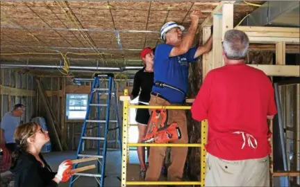  ?? CHAD FELTON — THE NEWS-HERALD ?? Dr. Susan Miller, far left, and Dr. Laura Shepardson, in cap, watch Lake-Geauga Habitat for Humanity volunteer Joe Fenske place slats of wood under a ceiling beam at the nonprofit’s Eastlake home constructi­on site on Sept. 23. Volunteer Rick O’Donnell...