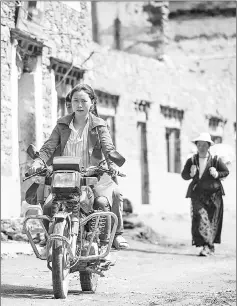  ??  ?? A woman riding a motorcycle on a street in Zhaba.