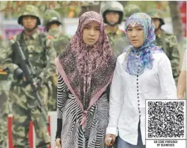  ??  ?? Mujeres de la etnia uigur vigiladas por militares chinos.