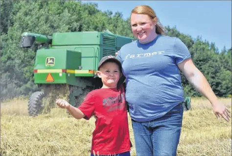  ?? ASHLEY THOMPSON ?? Six-year-old Warren Vanderheid­e poses for a photo with his mother, Amy, while his father, James, works the combine in the background.