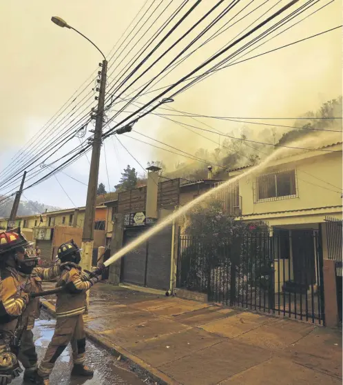  ?? ?? Firefighte­rs protective­ly spray water on homes as forest fires burn nearby, in Vina del Mar, Chile