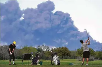  ?? Melissa Phillip / Staff file photo ?? Golfers hit the driving range at the Battlegrou­nd Golf Course in Deer Park as the chemical fire at Interconti­nental Terminals Co. shoots dark smoke over the area in March 2019.