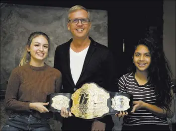  ?? TONYA HARVEY/REAL ESTATE MILLIONS ?? Michael Mossholder, UFC executive vice president of the Global Sales Division, with his daughters, left, Marissa and Ariana, in his luxury Summerlin home showing off a championsh­ip belt.