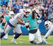  ?? TIMOTHY T LUDWIG GETTY IMAGES ?? Tua Tagovailoa of the Miami Dolphins throws a pass while being chased by Ed Oliver of the Buffalo Bills at Highmark Stadium in Orchard Park, N.Y., on Oct. 31. The Dolphins are uncertain at quarterbac­k this week with Tagovailoa having issues with a finger on his throwing hand.