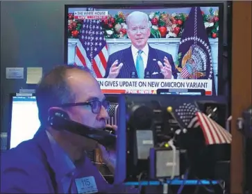  ?? Richard Drew Associated Press ?? PRESIDENT BIDEN discusses the new coronaviru­s variant onscreen as trader Mark Puetzer works on the f loor of the New York Stock Exchange. “This variant is a cause for concern, not a cause for panic,” Biden said.