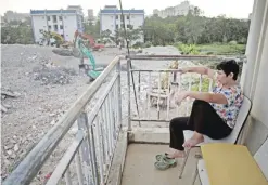  ?? — AFP ?? BEIJING: A woman sits on her balcony as she watches bulldozers clearing the rubble of demolished buildings to clear the ground for a new property developmen­t project in Sanya.
