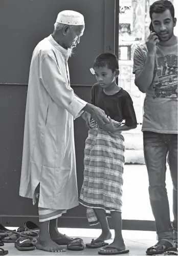  ?? MACKY LIM ?? PRAY TIME. A Muslim man secures the malong of a young boy before they head inside the mosque in Barangay 23-C Isla Verde in Davao City for the afternoon prayer.