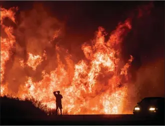  ?? The Associated Press ?? In this Dec. 6 file photo, a motorist on Highway 101 watches flames from the Thomas fire leap above the roadway north of Ventura, Calif. The huge wildfire that burned hundreds of homes in Santa Barbara and Ventura counties is now the largest in...