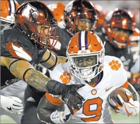  ?? Timothy D. Easley ?? The Associated Press Clemson running back Travis Etienne tries to elude the tackle of Louisville linebacker James Hearns, left, in the third-ranked Tigers’ 47-21 road victory Saturday over the No. 14 Cardinals. Clemson moved up one spot to No. 2 in The...